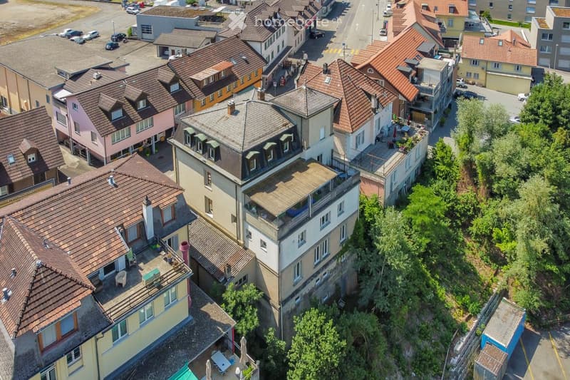 Aerial view of a residential area with multiple houses featuring red-tiled roofs, various architectural styles, and surrounding greenery.