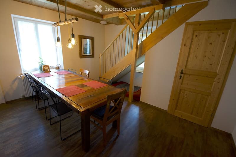 Bright dining area with wooden dining table, chairs, and a staircase leading to an upper level.
