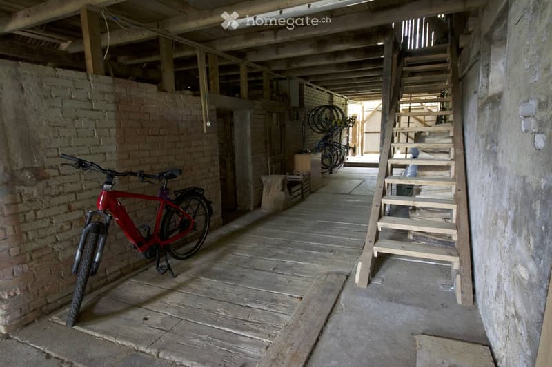 A rustic wooden hallway with exposed brick walls, a wooden staircase leading upwards, and a red electric bicycle parked on the left side.