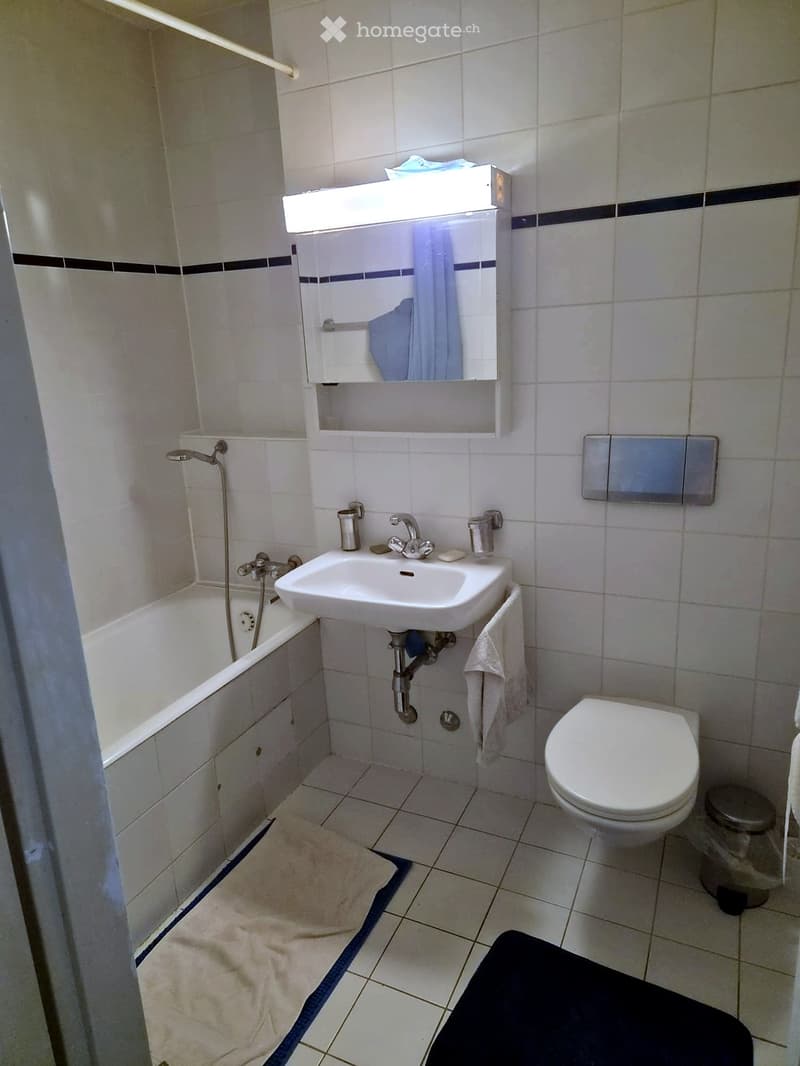 A small bathroom with a bathtub, sink, toilet, mirror, and towels.