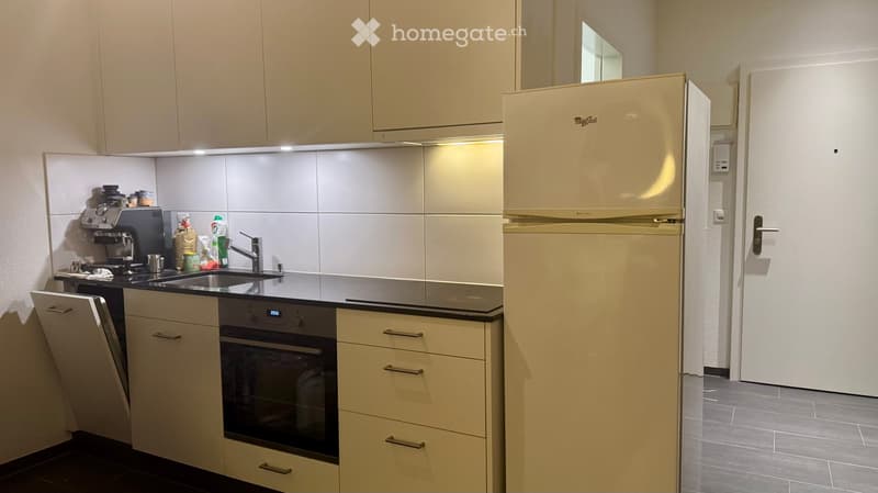 Modern kitchen with light-colored cabinets, stainless steel appliances, and a black countertop.