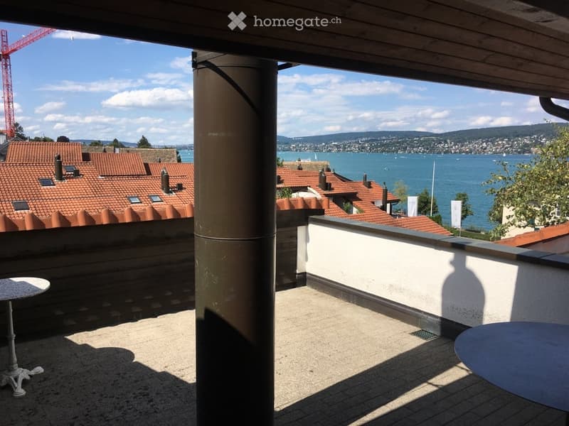 Balcony with a scenic view of a lake and surrounding rooftops, featuring a round table and a column.