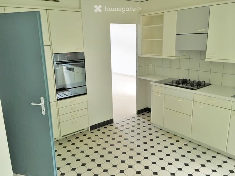 Modern kitchen with white cabinets, black and white hexagonal tile floor, built-in oven, dishwasher, and gas stove.