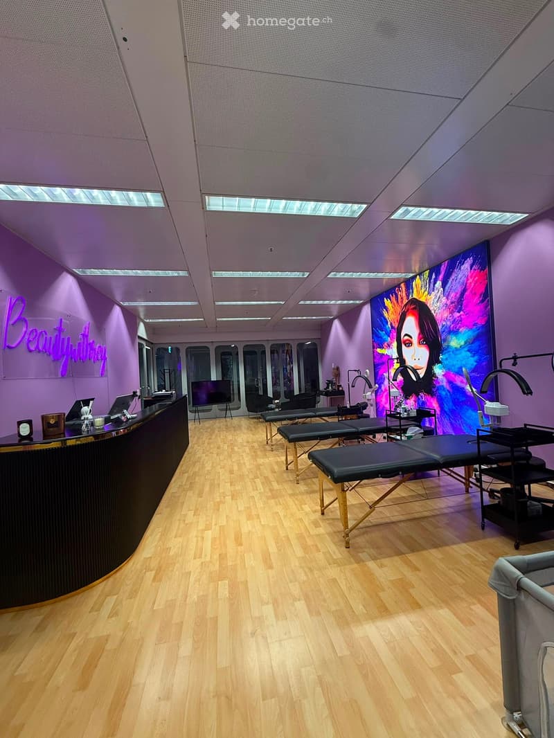 Modern beauty salon with wooden flooring, reception desk, treatment tables, mirrors, and colorful artwork.
