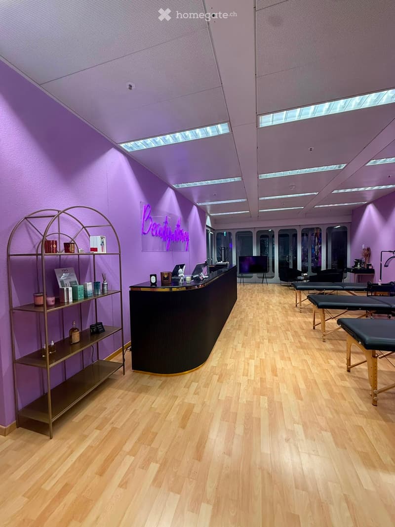 A modern beauty salon with purple walls, wooden flooring, a reception counter, shelves with products, and several massage chairs.