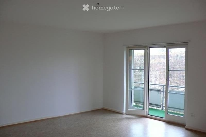 Empty room with light-colored walls, wooden floor, and large sliding glass doors leading to a balcony.