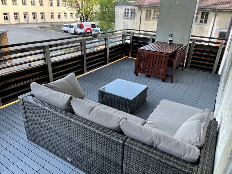 Balcony with wicker sofa, glass coffee table, wooden dining table, and chairs.