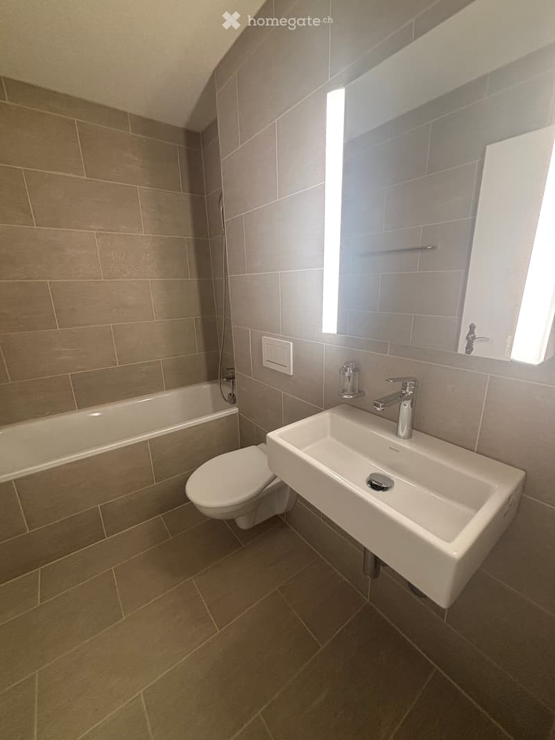 Modern bathroom with beige tiled walls and floor, white toilet, sink, and faucet.
