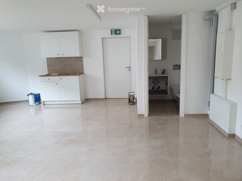 Empty room with white cabinets, a sink, and a door leading to a small bathroom area. The space features tiled flooring and white walls.
