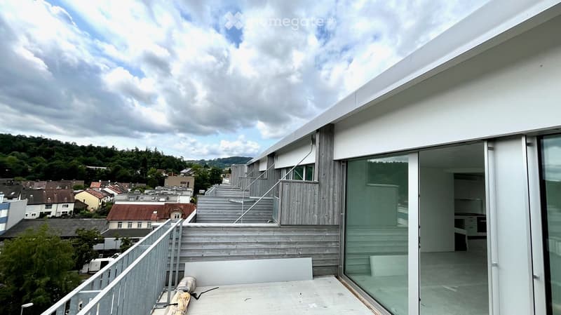 Modern rooftop terrace with wooden decking, metal railing, and expansive view of the town and surrounding greenery.