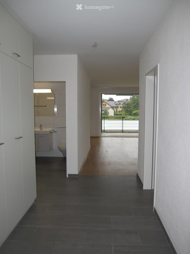 Empty hallway with white walls, gray tiles, white cabinets, and a balcony with a glass railing.