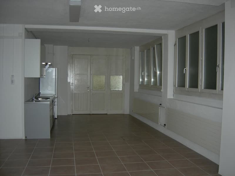 Empty room with tiled floor, white walls, and large windows. No furniture or equipment visible.