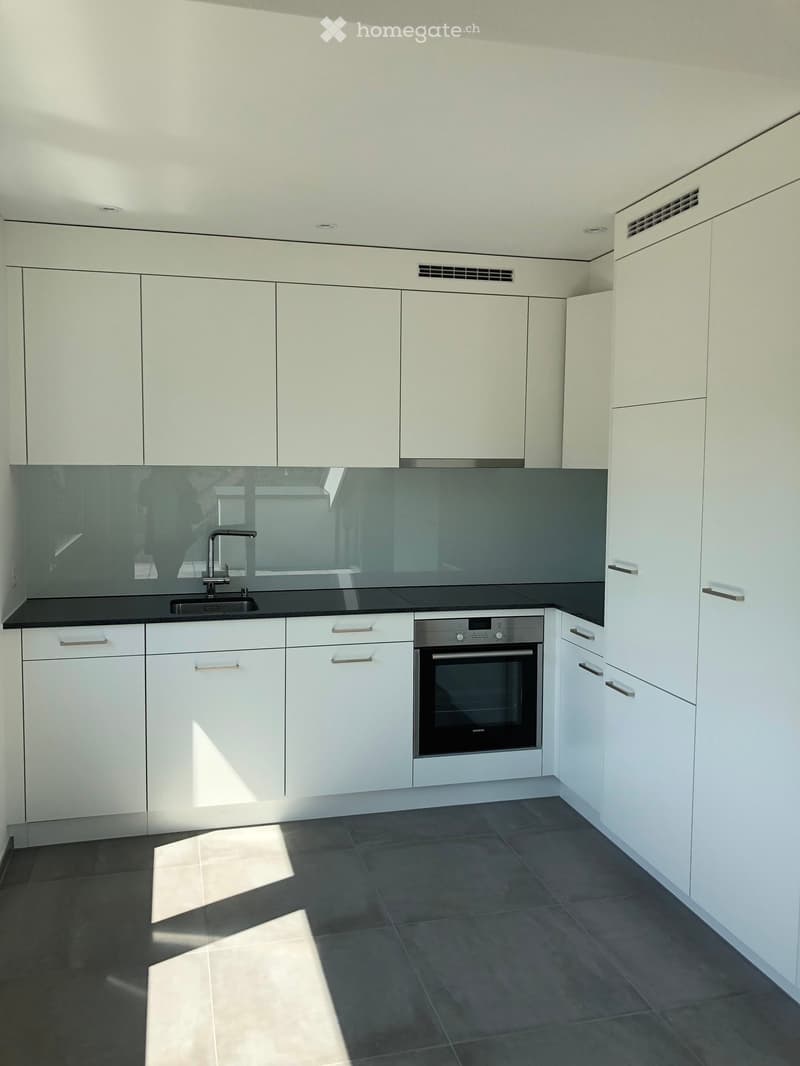 Modern kitchen with white cabinets, black countertops, and stainless steel appliances, including a sink and oven.