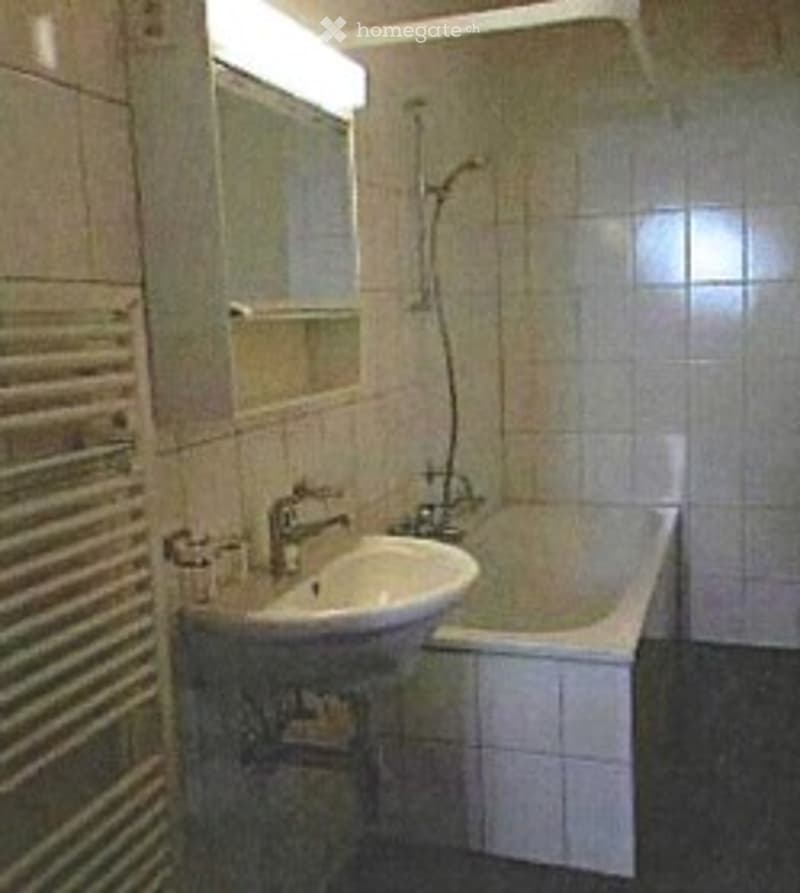 Modern bathroom with white tiled walls and floor, a sink with a chrome faucet, a bathtub with a showerhead, a towel rack, and a mirror above the sink.