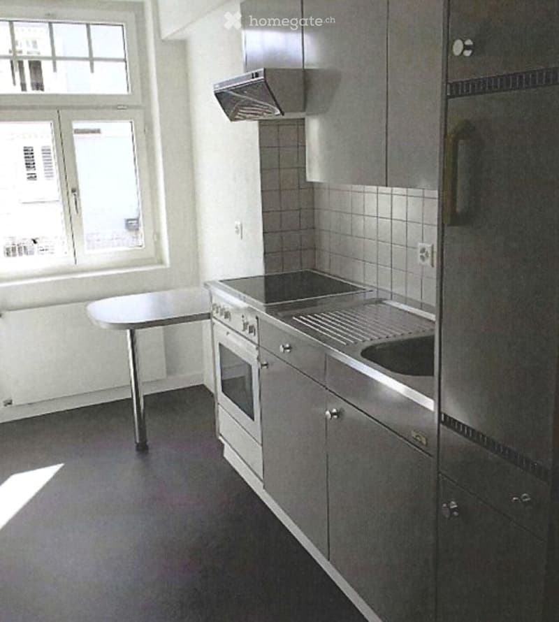 Modern kitchen with stainless steel appliances, including a stove, oven, and sink, along with grey cabinets and a small table near the window.