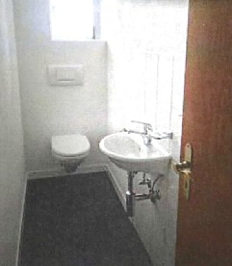 Small bathroom with white tiled walls, a toilet, a sink with a faucet, and a dark grey carpeted floor.