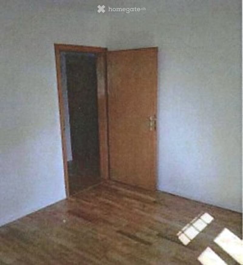 Empty room with wooden flooring, white walls, and a single wooden door.