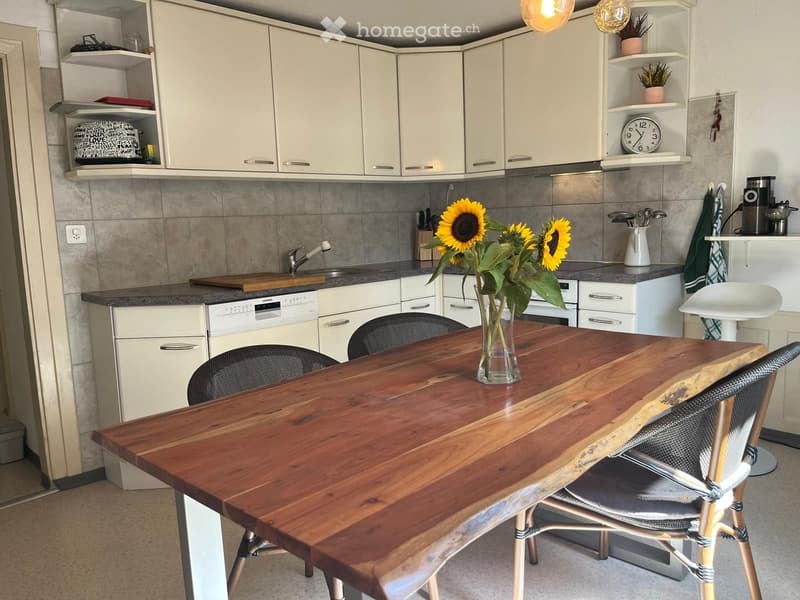 Modern kitchen with white cabinets, a wooden dining table, four chairs, a vase with sunflowers, a dishwasher, and a sink.