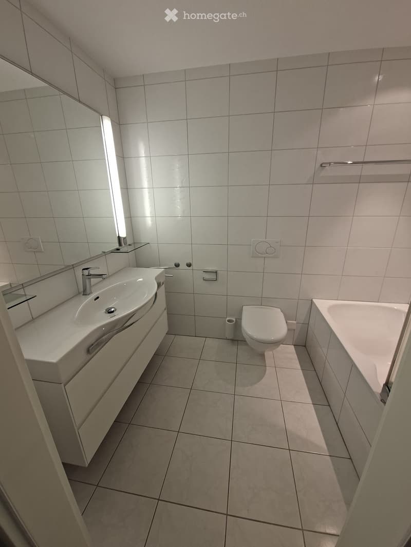 Modern bathroom with tiled walls and floor, featuring a sink, toilet, bathtub, and mirror.