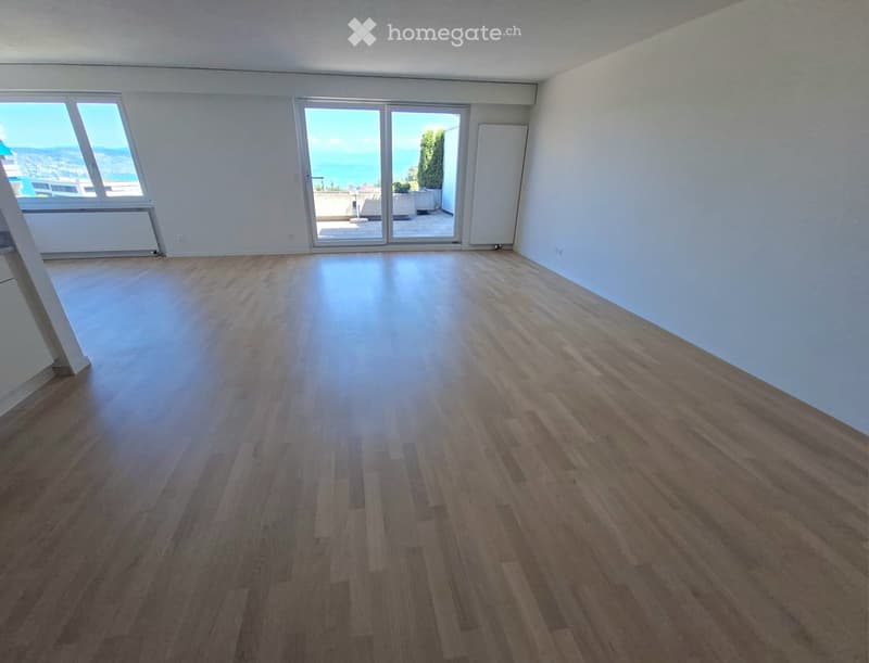Empty room with wooden flooring, large windows, and sliding glass doors leading to a balcony with a sea view.