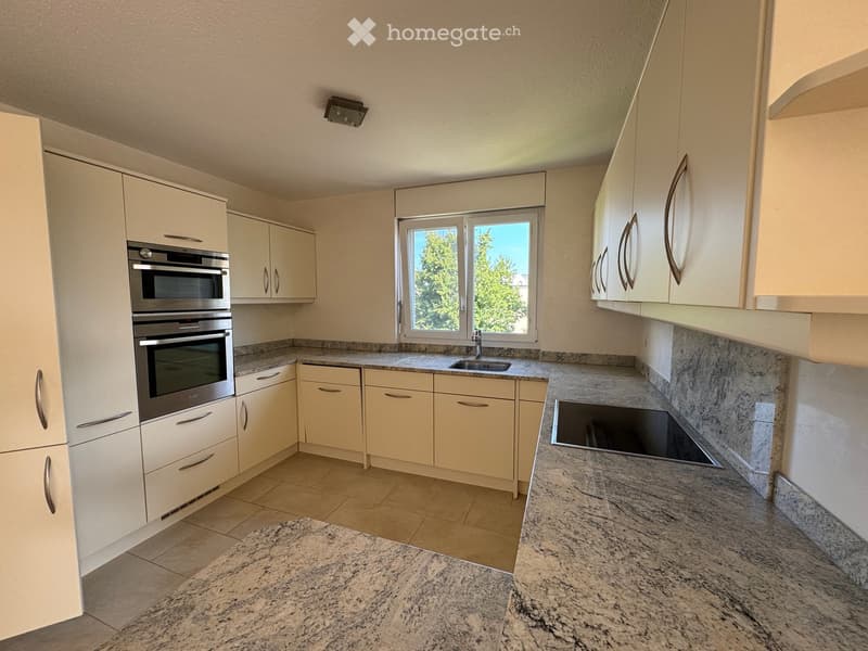 Modern kitchen with light-colored cabinets, granite countertops, and stainless steel appliances including an oven and sink.