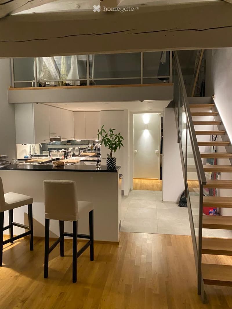 Modern kitchen with white cabinets, black countertop, bar stools, and a staircase leading to an upper level.