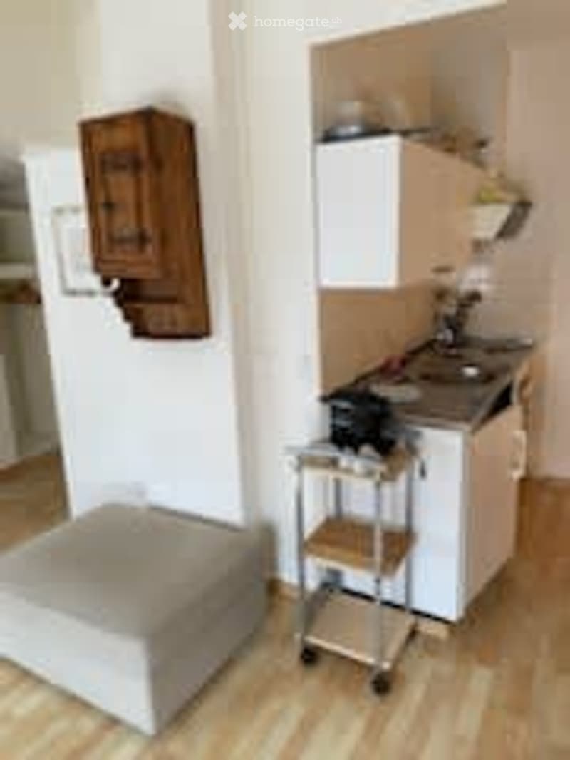 Small kitchen area with a stool, sink, and a cart. The space includes a kitchen cabinet and a faucet.
