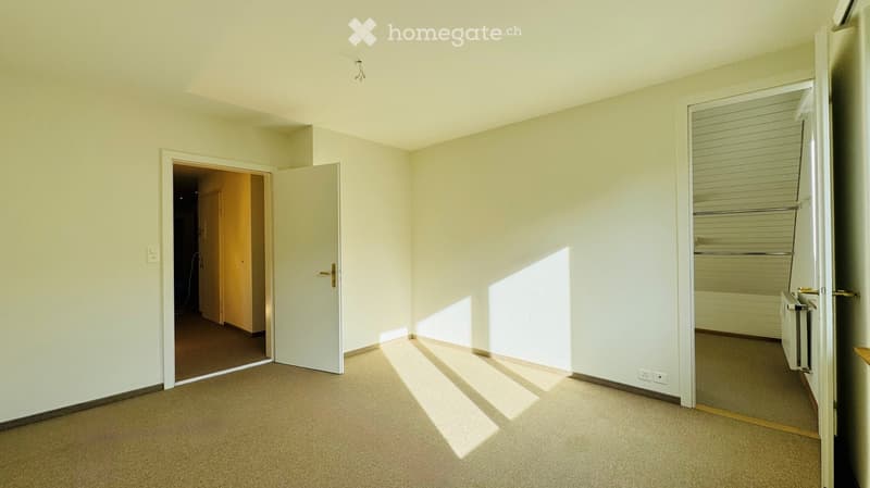 Empty room with light-colored walls, carpeted floor, and two open doors leading to adjacent spaces.