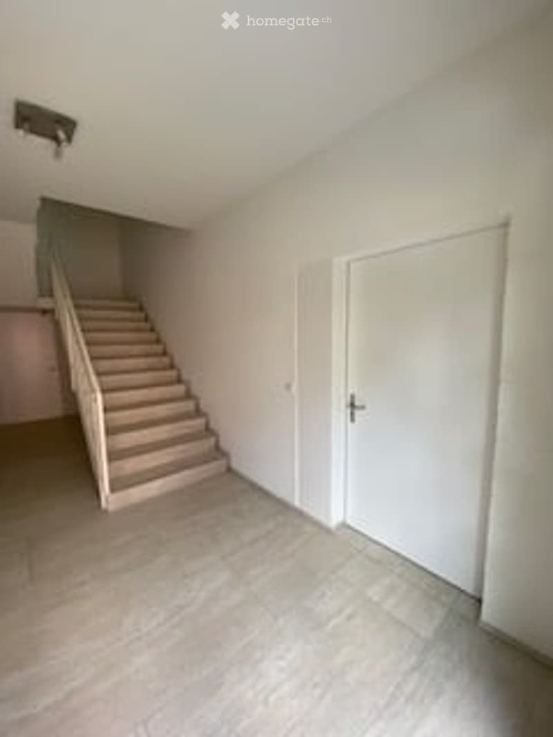 Empty hallway with a staircase leading upwards, white walls, and a closed door.