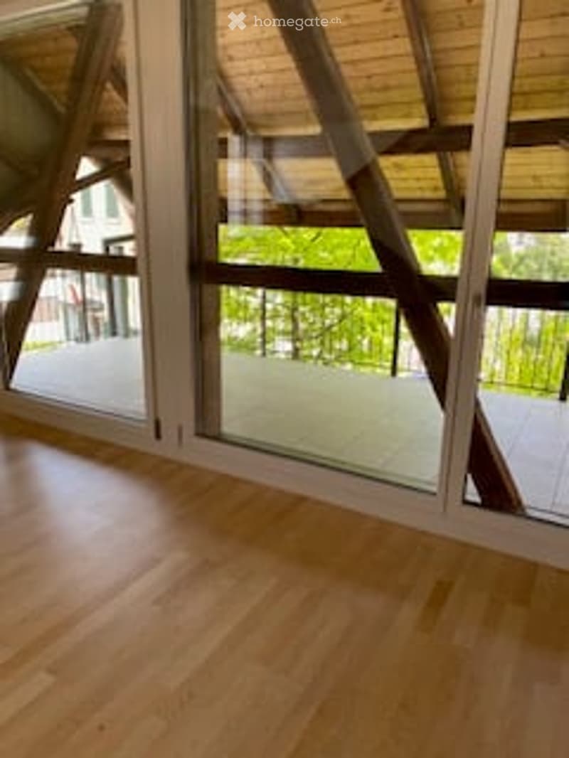 Empty room with wooden flooring and large glass windows, allowing natural light to fill the space.