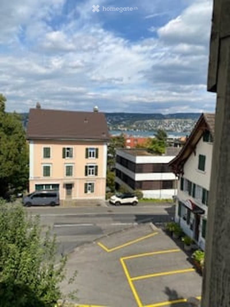 Multi-story residential building with a flat roof and multiple windows, surrounded by a parking lot with several cars.