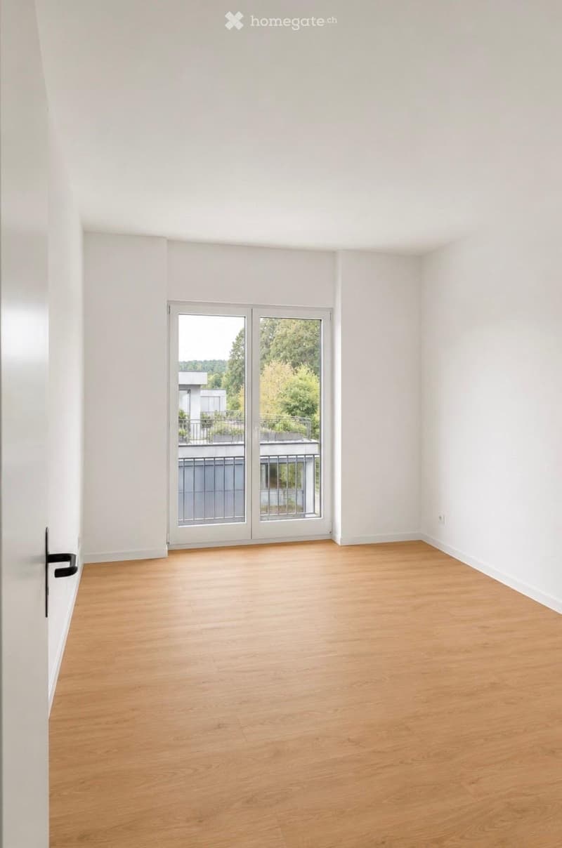 Empty room with light wooden flooring and white walls, featuring a large sliding glass door leading to a balcony with a metal railing.