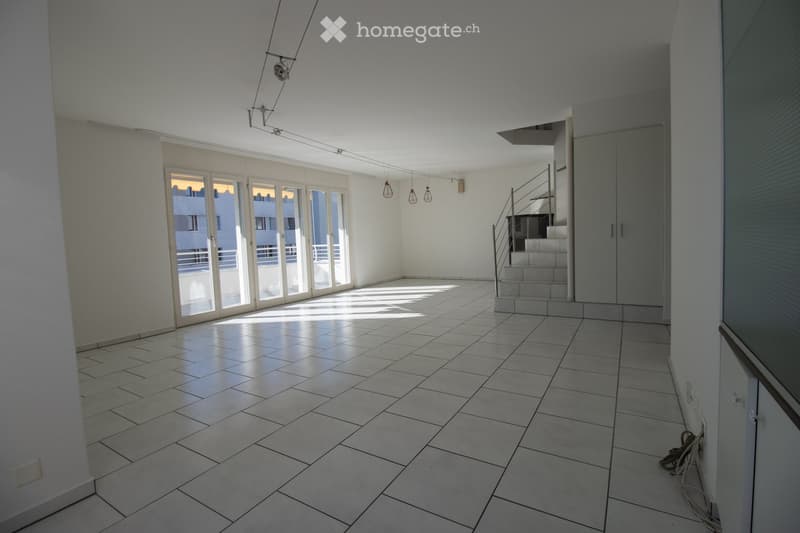 Empty room with tiled floor, white walls, large glass doors leading to a balcony, and a staircase leading to another level.