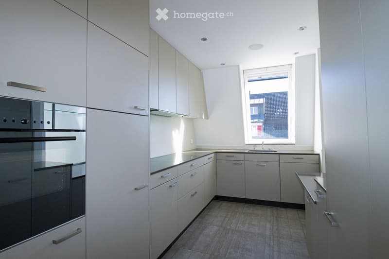 Modern kitchen with light grey cabinets, stainless steel oven, and a window overlooking the street.