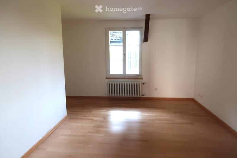 Empty room with wooden flooring, white walls, and a single window with a radiator below it.