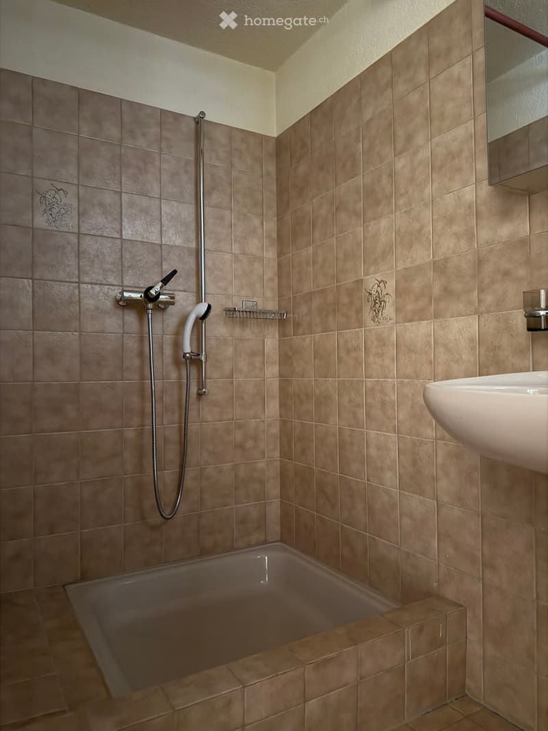 Modern bathroom with beige tiled walls and floor, featuring a bathtub, a modern faucet with a handheld showerhead, a sink, and a mirror above the sink.