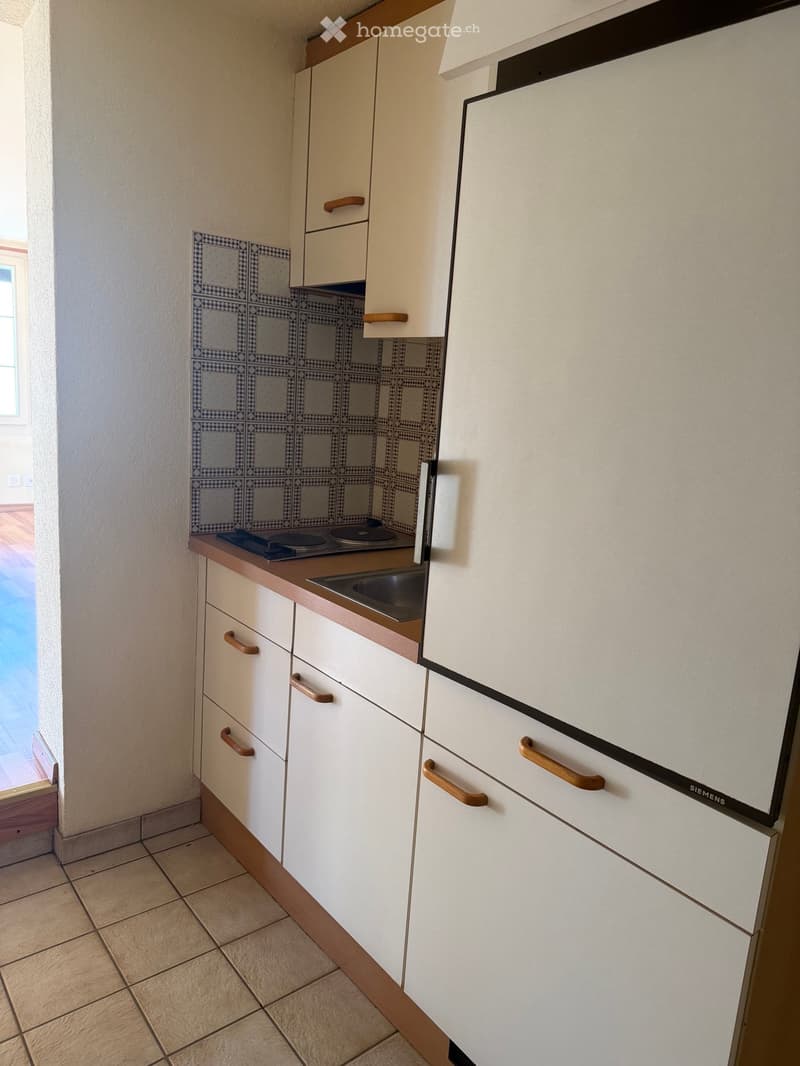 Modern kitchen with white cabinets, wooden handles, a sink, and a stove. The backsplash features a blue and white tile design.