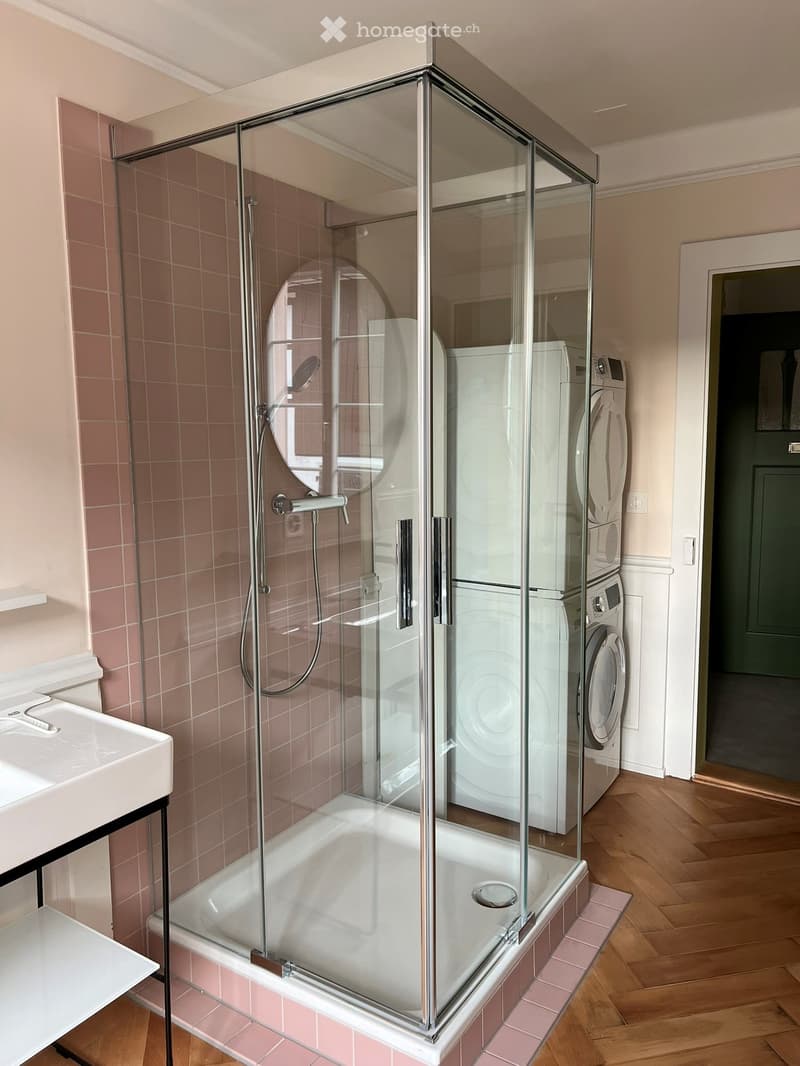 Modern bathroom with a glass-enclosed shower, bathtub, sink, and stacked washing machine and dryer unit.