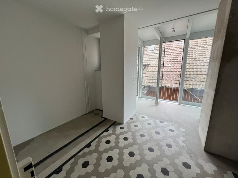 Hallway with hexagonal tile flooring, leading to a balcony area with glass doors and a view of a tiled roof.