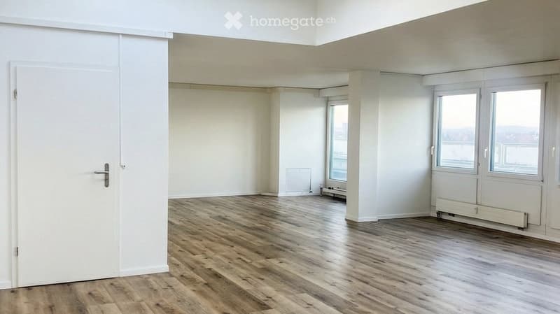Empty room with wooden flooring, white walls, and large windows offering a view. No furniture or equipment present.