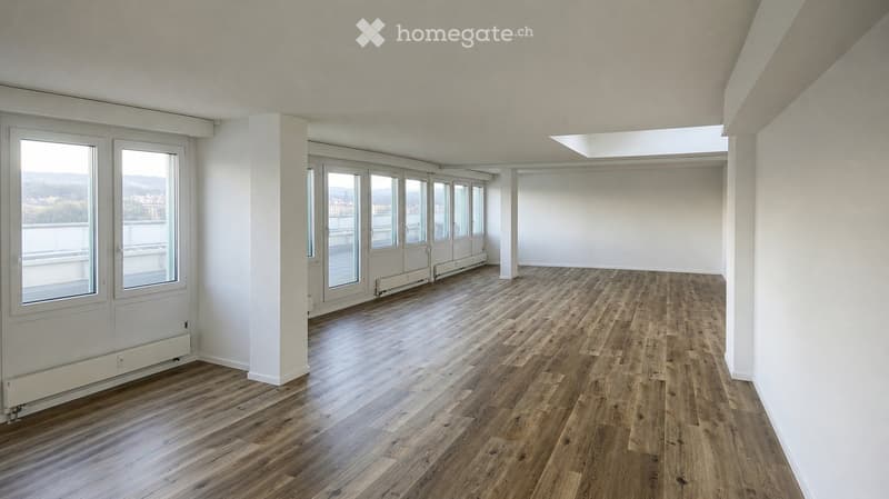 Empty room with wooden flooring, white walls, large windows, and a balcony area visible through the glass doors.
