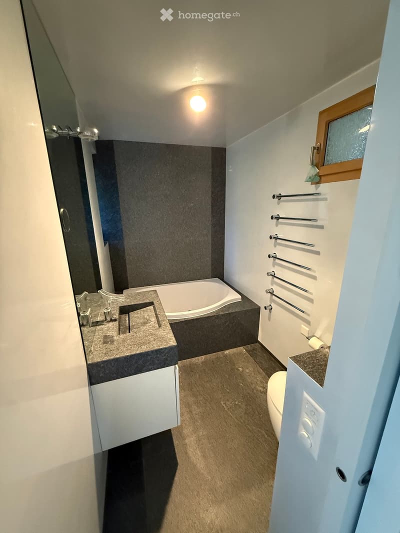 Modern bathroom with a sink, bathtub, toilet, and towel rack. Features a sleek design with a dark countertop and white cabinetry.