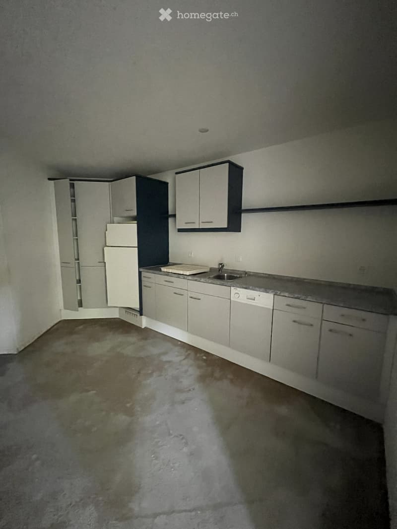 Empty kitchen with white cabinets, a sink, and a dishwasher, showing a wet floor with water pooling.