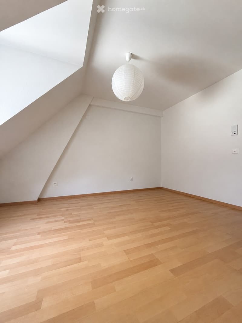 Empty room with wooden flooring and white walls, featuring a single hanging light fixture and electrical outlets.