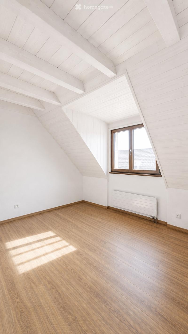 Empty attic room with wooden flooring, white walls, slanted wooden ceiling, and a single window with brown frame.