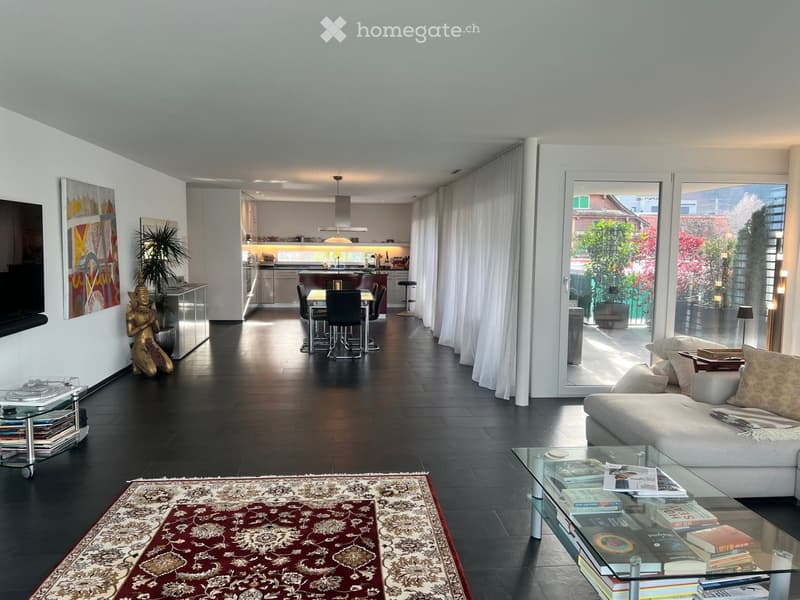 Open layout, sleek white furnishings, large glass doors, elegant rug, contemporary art, modern kitchen, dining area, large balcony with outdoor plants