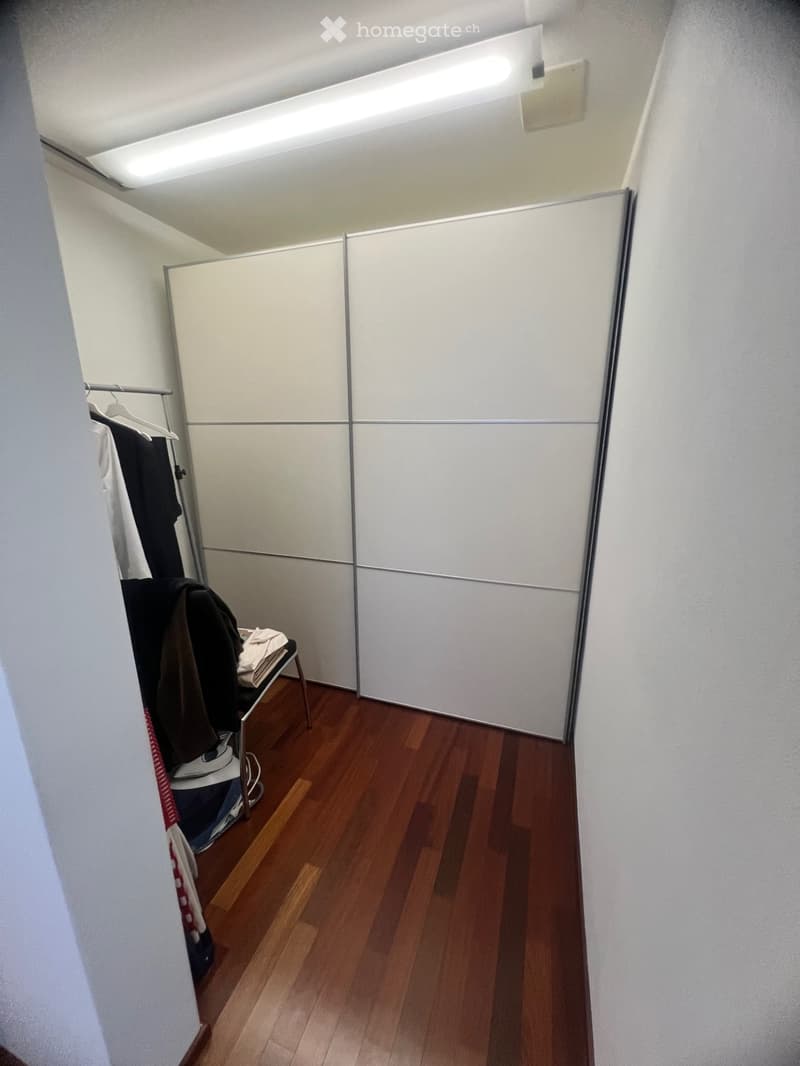 Walk-in closet with wooden floor, white sliding doors, clothes hanger, white clothing