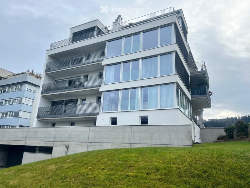 modern multistory building, large windows, several balconies, concrete wall, green lawn