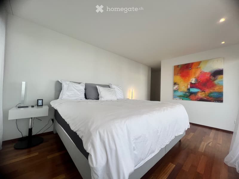 A modern bedroom with a bed, side table, and a painting on the wall