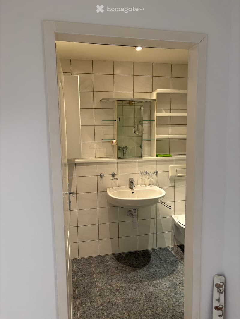 Modern bathroom with beige tiles, a sink, toilet, mirror, and glass shower enclosure.